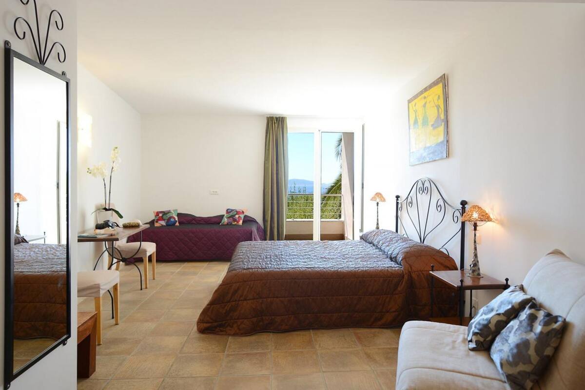Ein Hotelzimmer mit Bett, Schreibtisch, Stuhl, Sofa und einem Balkon mit Blick.