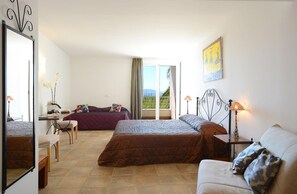 Habitación de hotel con cama, escritorio, silla, sofá y balcón con vistas.