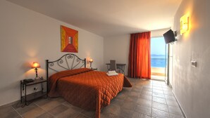 Une chambre à coucher comprenant un lit, une table de chevet, une lampe, un tableau, une chaise, une table et une vue sur la mer par une fenêtre.