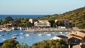 Un port de plaisance avec de nombreux bateaux, un grand bâtiment à étages et un paysage vallonné en arrière-plan.