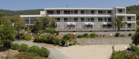 A modern multi-story building with balconies, surrounded by landscaped gardens and a clear sky.