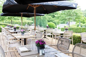 An outdoor dining area with wicker chairs and tables, umbrellas, and potted plants. - La Barrière de Transinne (Libin)