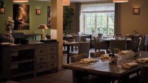 A restaurant with a wooden table set for dining, a cash register, and a plant.