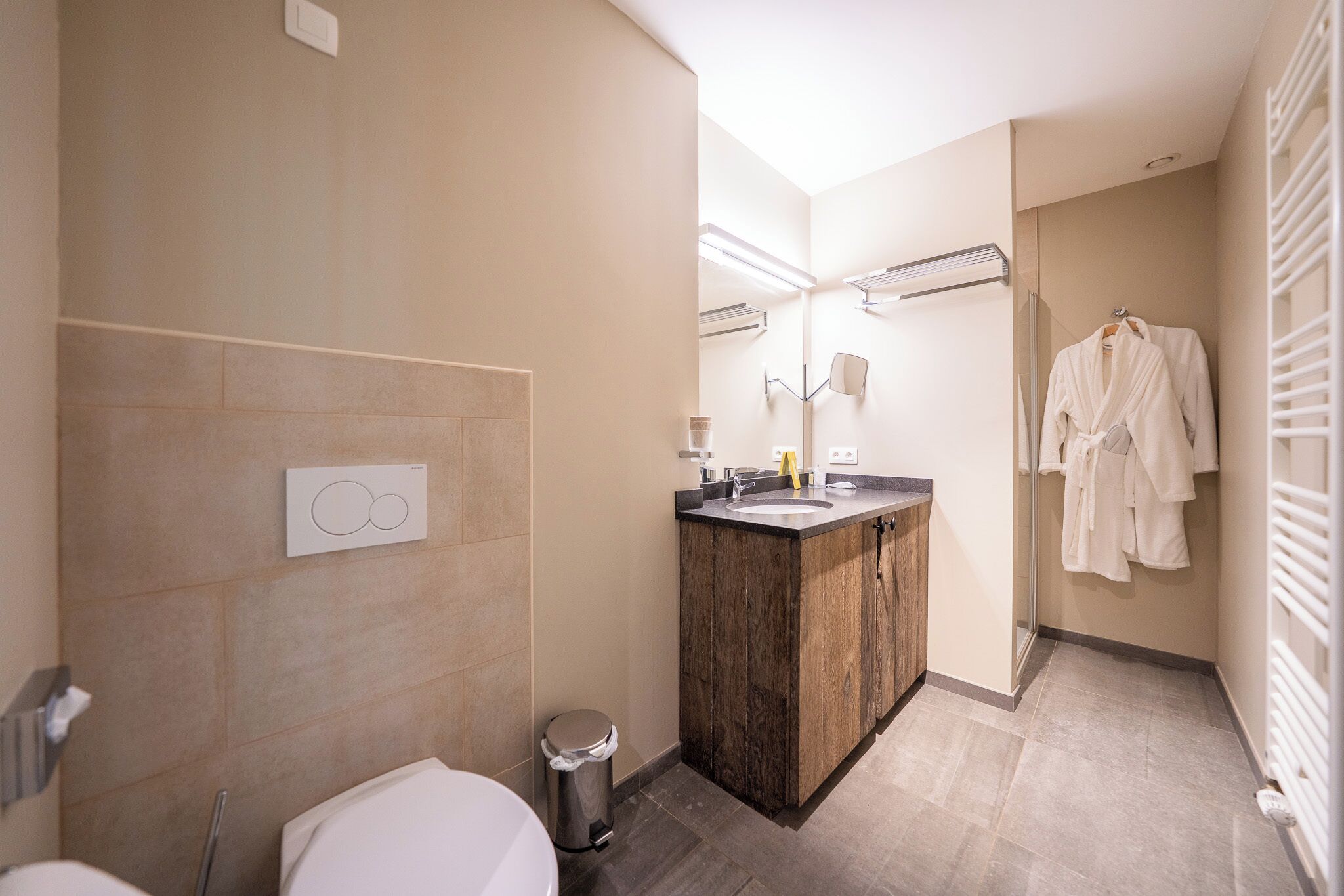 Une salle de bain moderne avec un meuble-lavabo en bois, un miroir, un porte-serviettes et des toilettes.