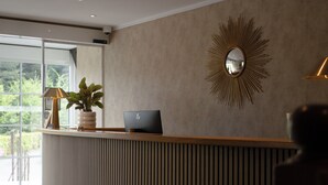 A reception desk with a laptop, a potted plant, and a sunburst mirror on the wall.