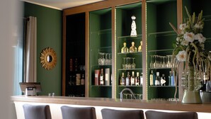 A bar area with a counter, chairs, and shelves with bottles and glasses.