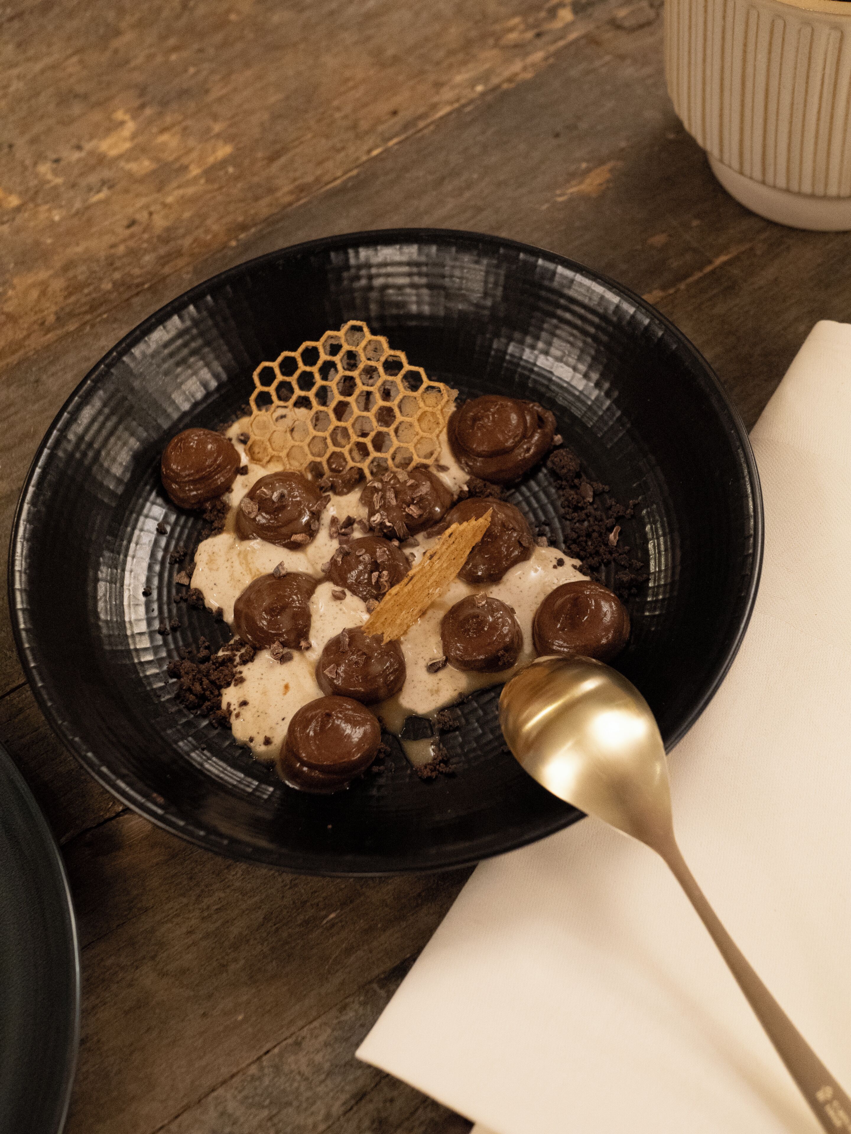 Un bol noir avec une cuillère, contenant des desserts au chocolat et une structure en forme de nid d’abeilles.
