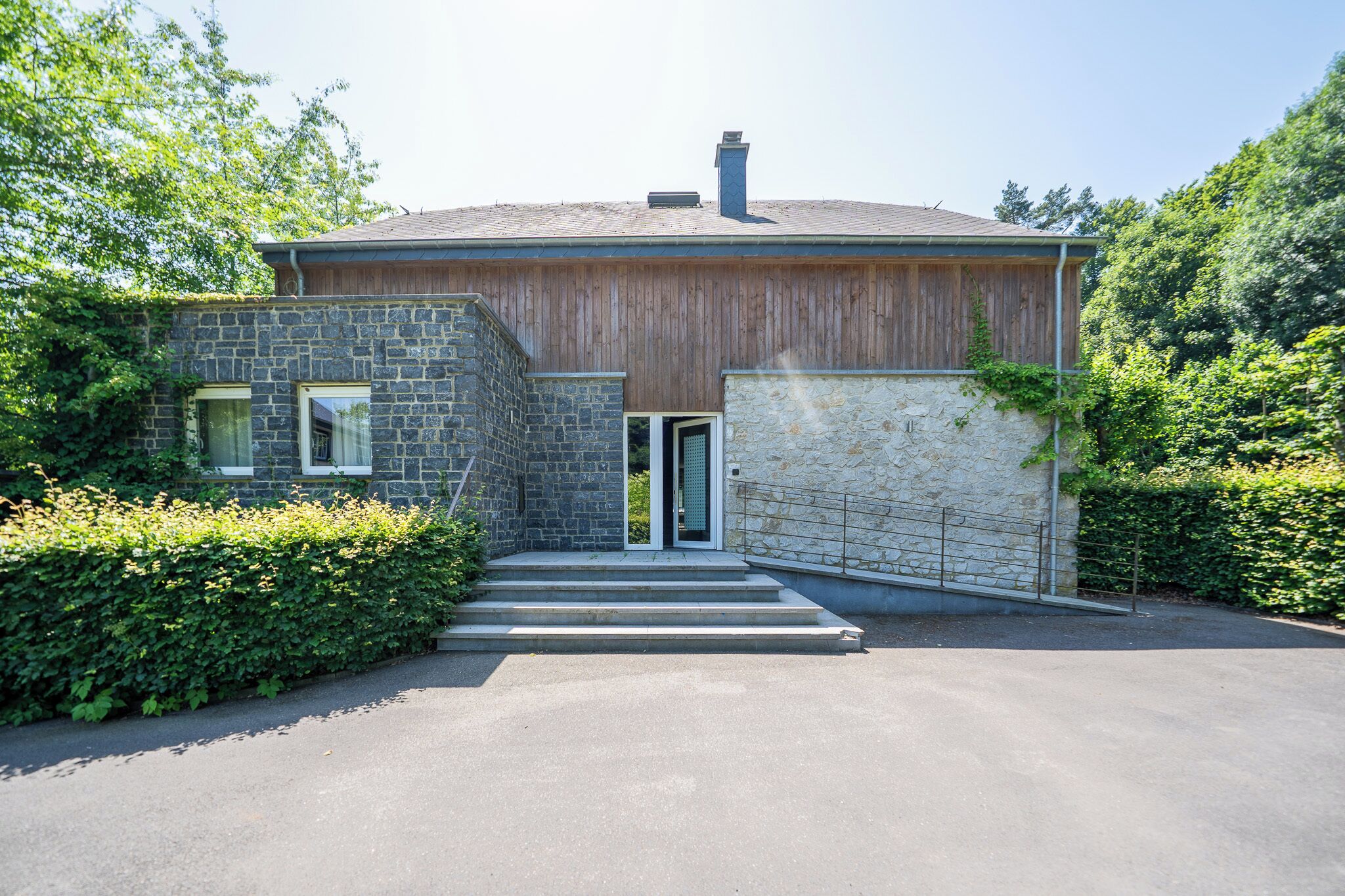 A modern house with a stone facade, wooden exterior, and a metal gate.