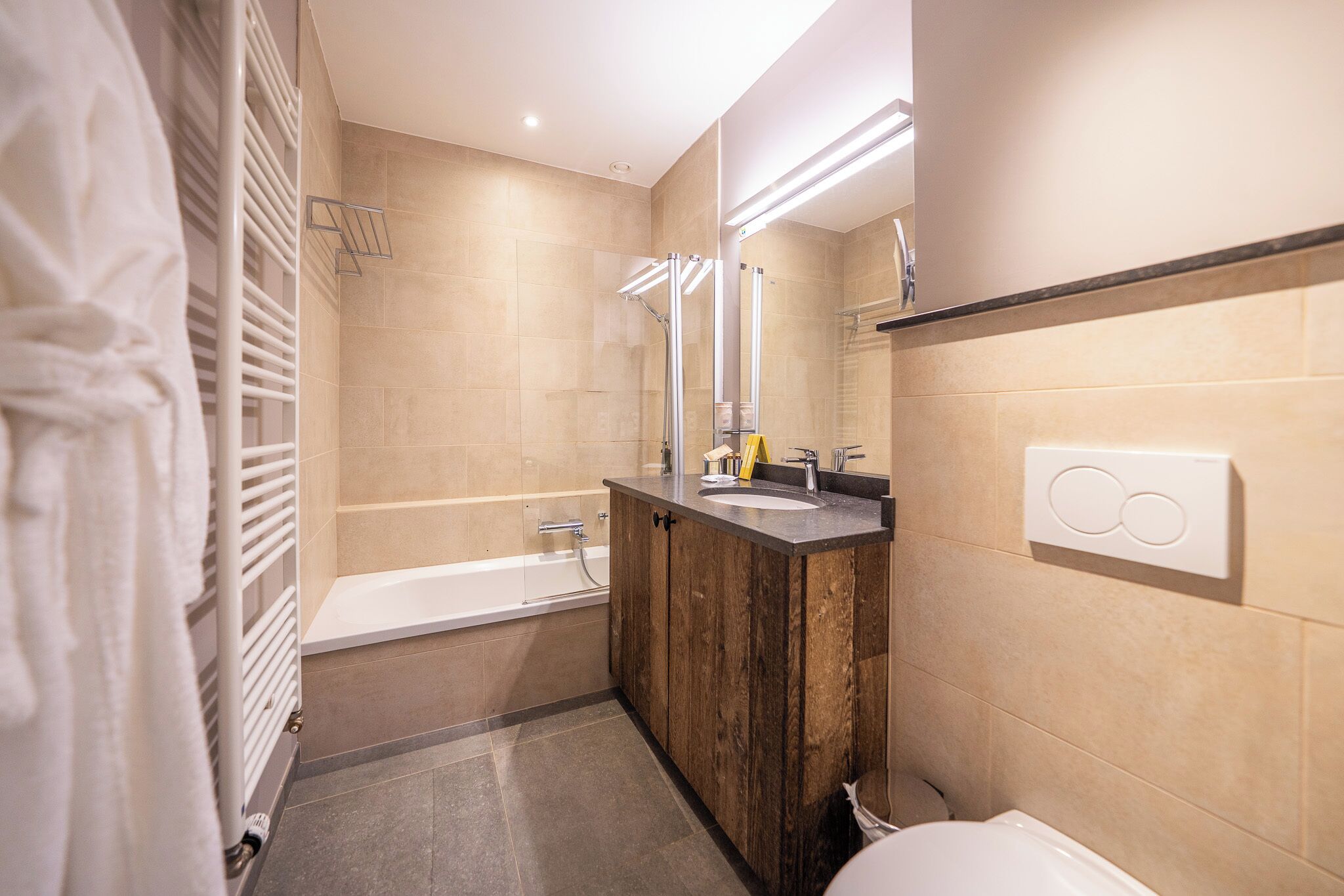 A modern bathroom with a bathtub, a wooden vanity, a large mirror, and a towel rack.