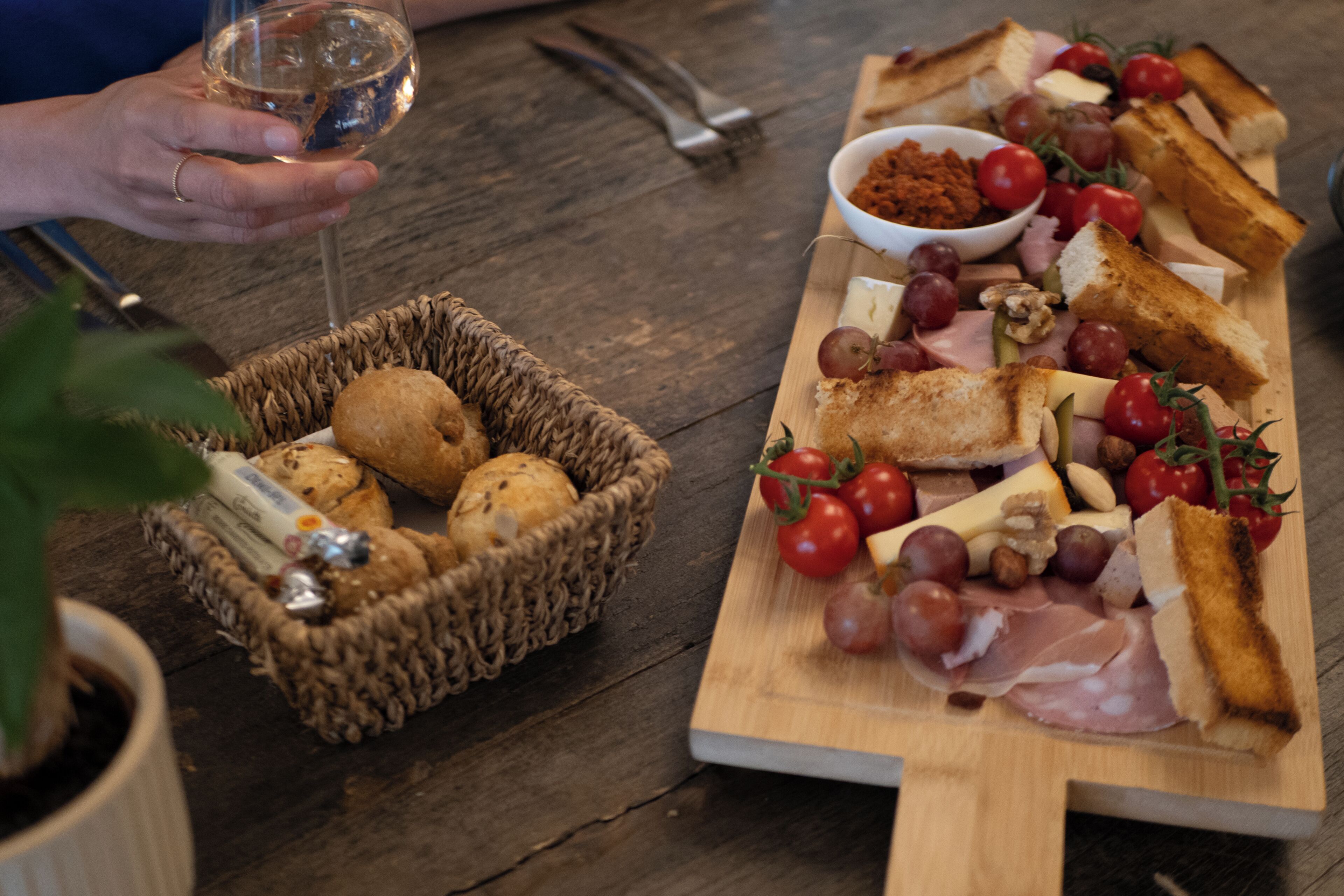 A wooden table with a charcuterie board, a basket of bread, and a glass of wine.