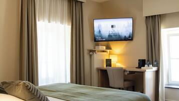 A hotel room with a bed, a desk, a television, and a window with curtains.
