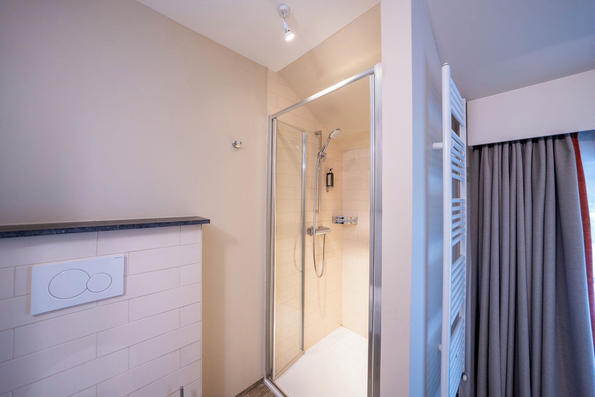 Un baño moderno con cabina de ducha de vidrio, pared con azulejos blancos y calefacción integrada.