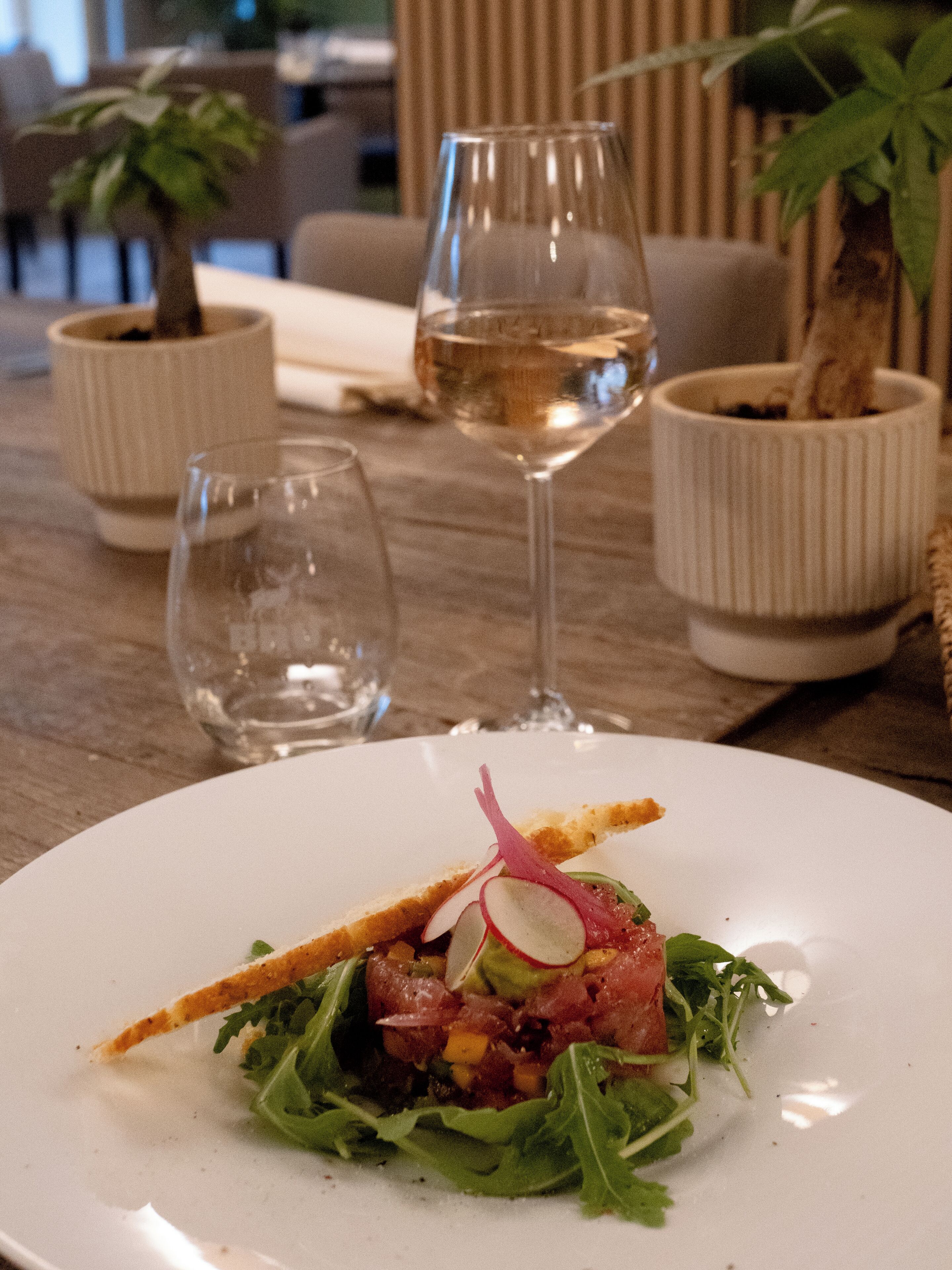 A dining table with a plate of food, two glasses, and two potted plants.