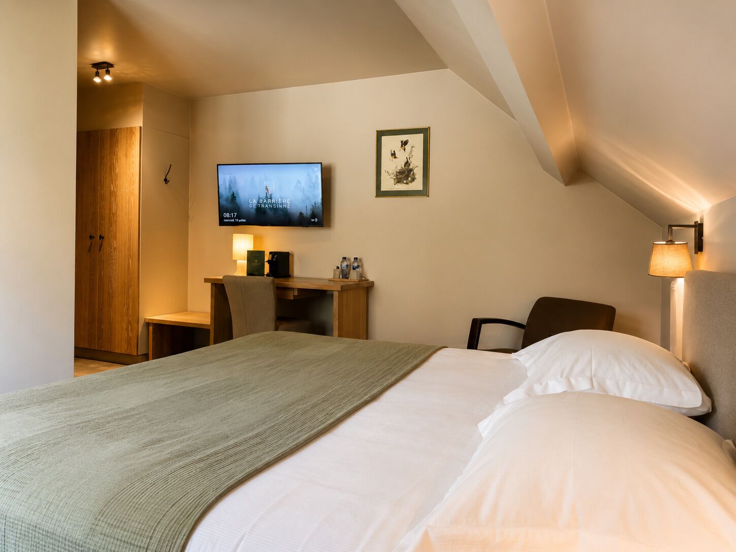 Een hotelkamer met een bed, een bureau met een computer, een televisie en een aan de muur hangend schilderij.