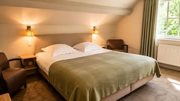 Habitació d'hotel amb un llit gran, dues làmpades laterals, una cadira, una taula petita i una finestra amb cortines.
