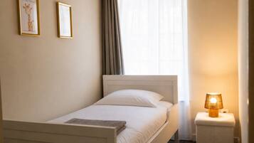 A single bed with a headboard, a bedside table with a lamp, and two framed pictures on the wall.