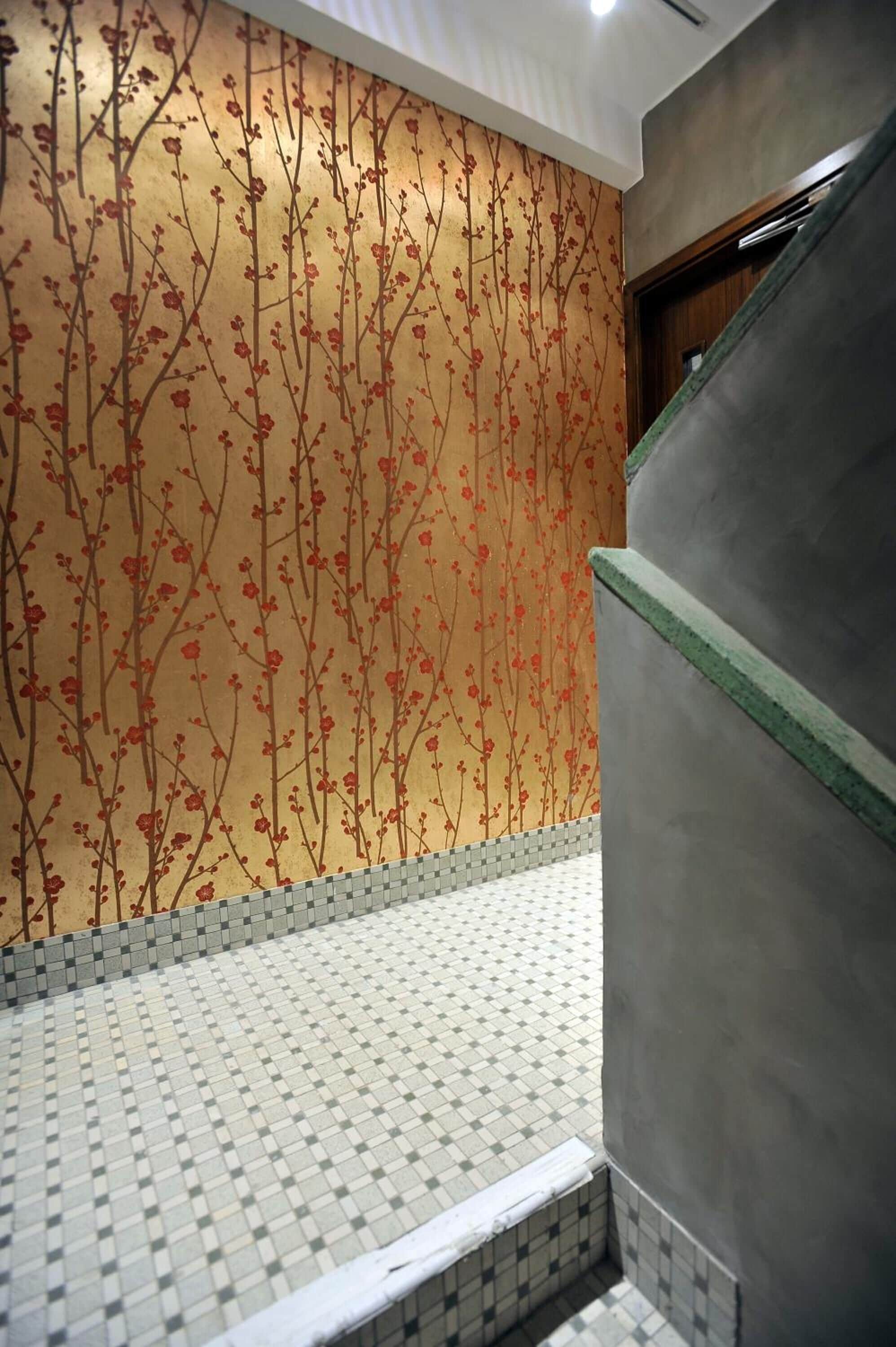 A bathroom with a tiled floor, a wall with a floral pattern, and a green-tinted shower area.