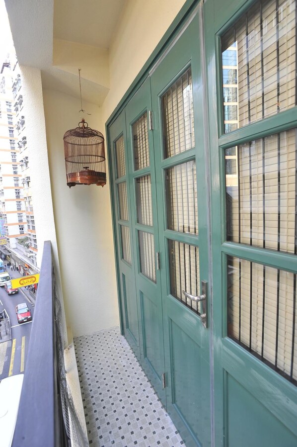 A balcony with a green door, a hanging birdcage, and a view of a busy street.
