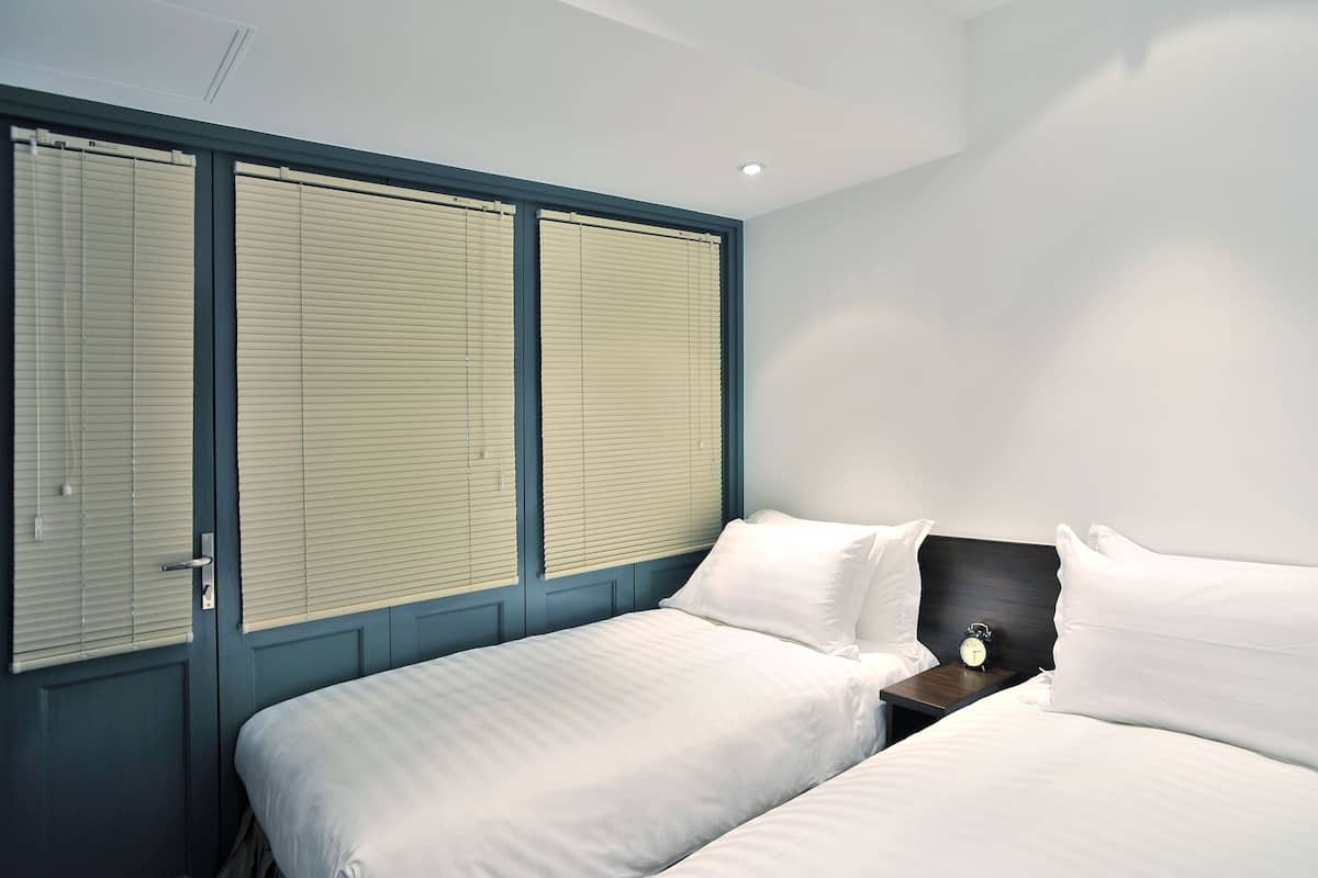 Un dormitorio con dos camas, una mesita de noche y una ventana con persianas.