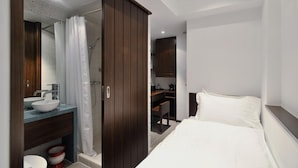 A modern bedroom with a large bed, a wooden wardrobe, a bathroom with a sink and shower, and a desk area. - Mingle Place by The Park (Hong Kong)