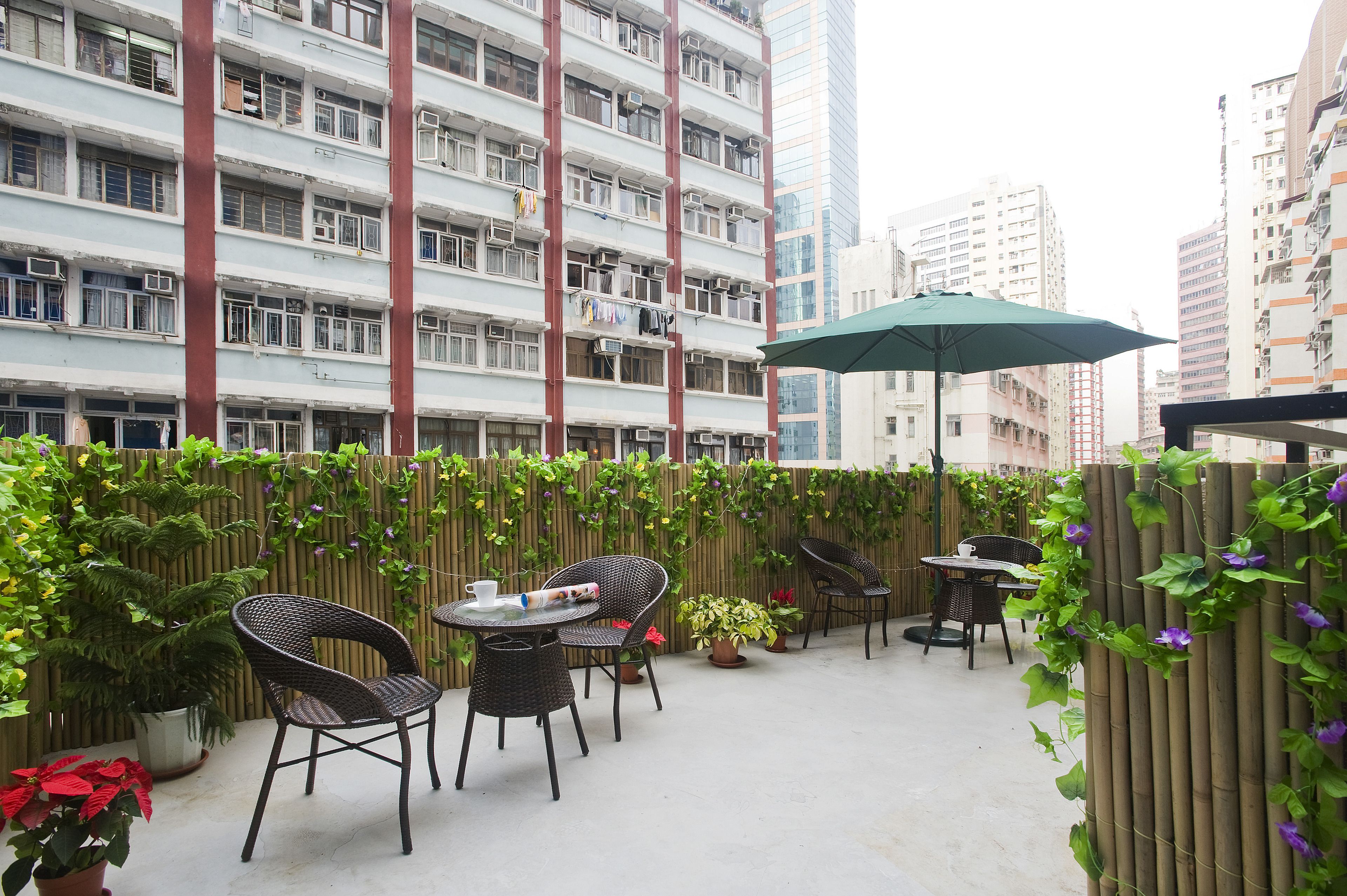 An outdoor patio with wicker chairs and tables, surrounded by a bamboo fence and potted plants.