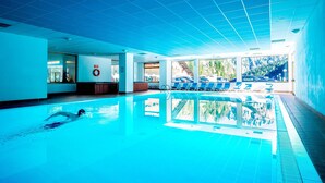 Una piscina interior con agua azul cristalina, un flotador en la pared y vistas a la montaña a través de amplias ventanas.