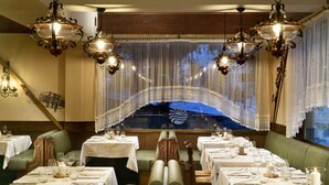 Un restaurante con varias mesas dispuestas para comensales, con vista a un puente a través de un cortinaje de encaje.