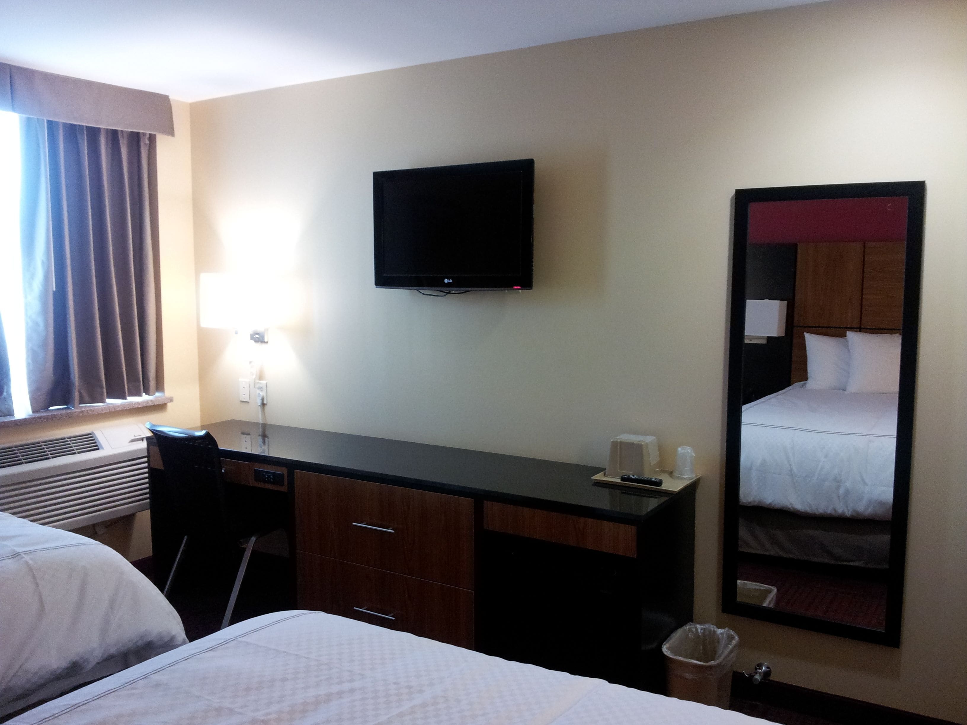 Ein Hotelzimmer mit Bett, Schreibtisch, Stuhl, Fernseher und Spiegel.