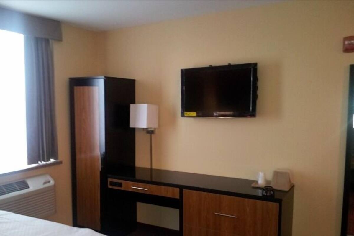 A hotel room with a bed, a desk, a television, and a window with curtains.