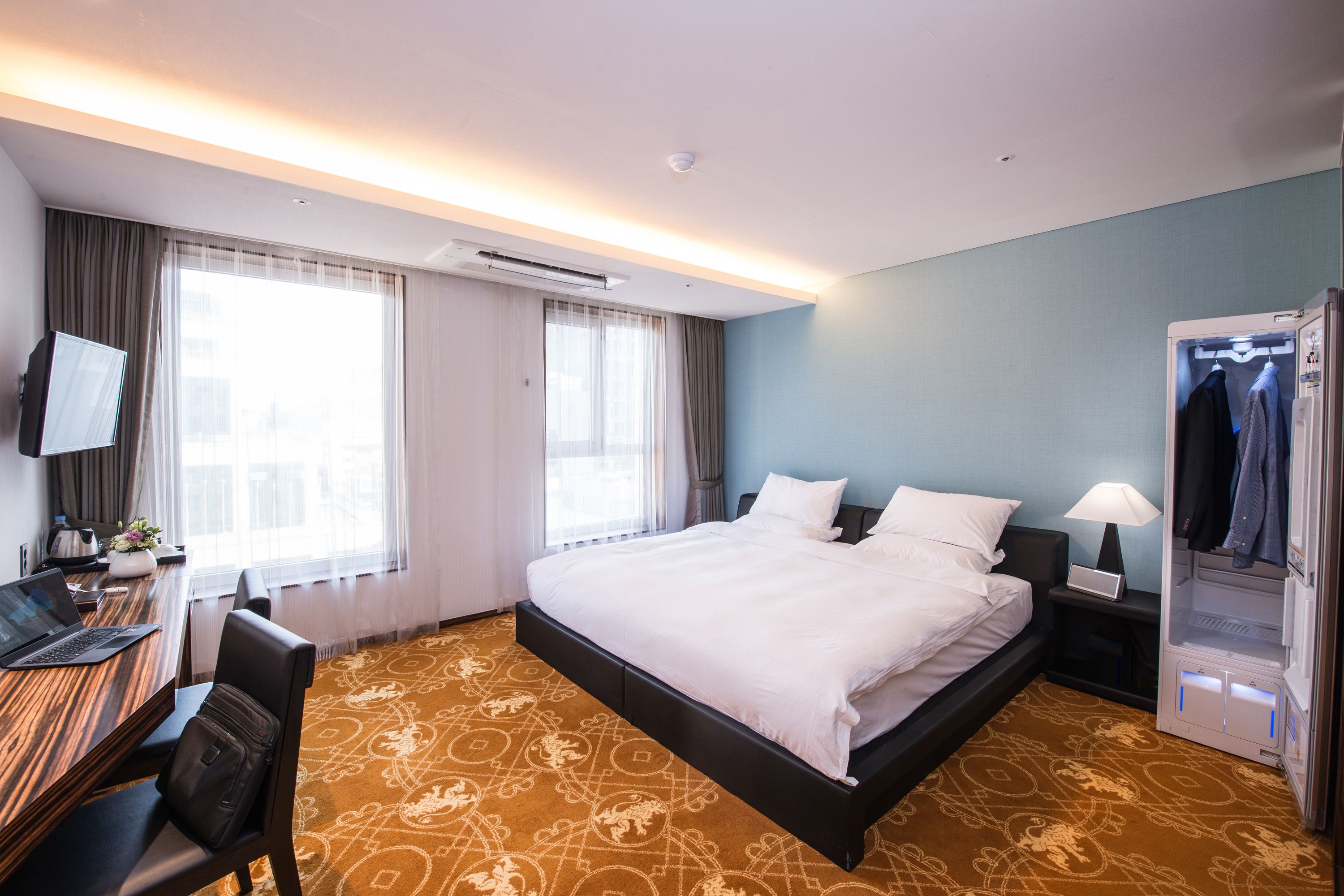 Une chambre d’hôtel avec un grand lit, un bureau avec un ordinateur portable, une télévision et un dressing.