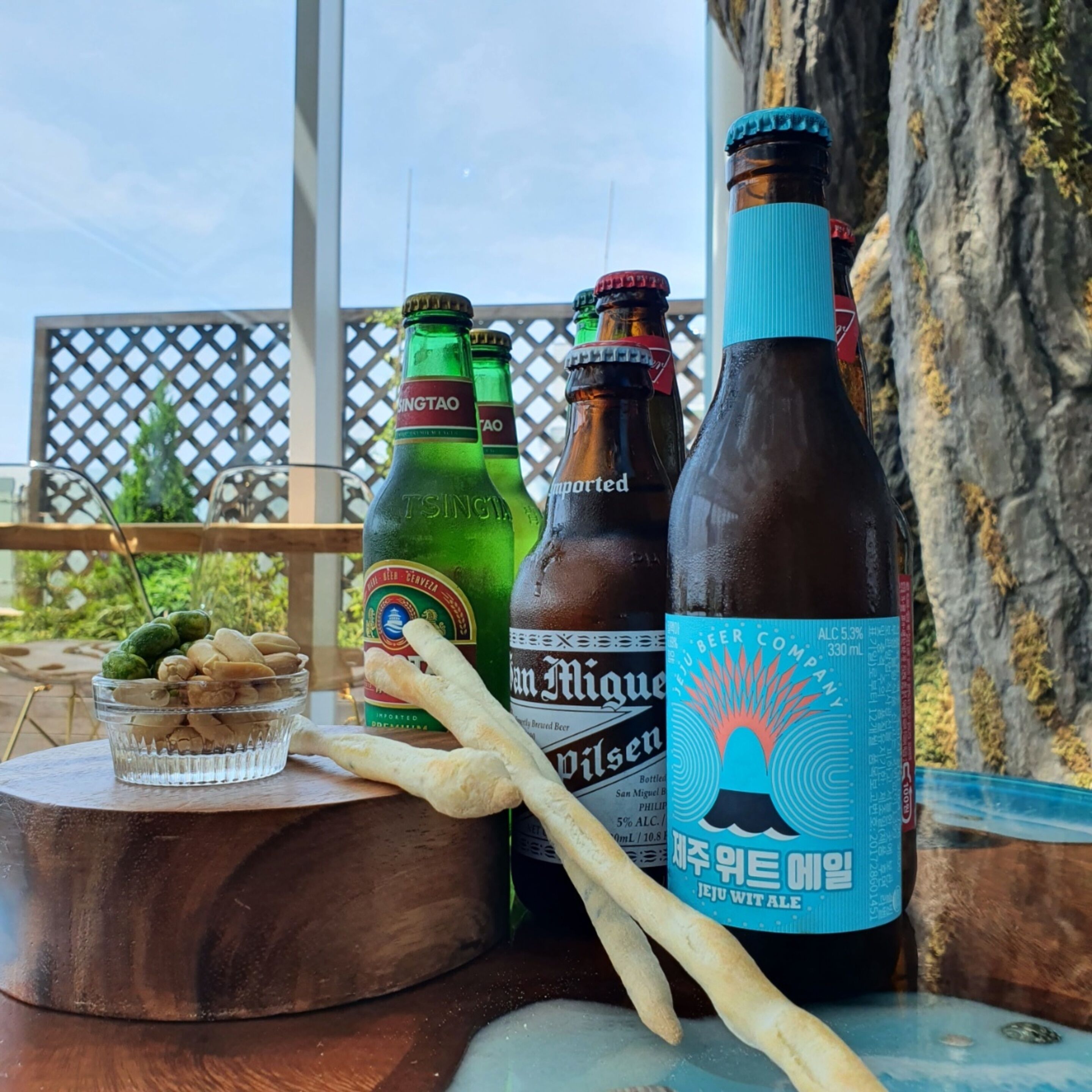 Une table avec des bouteilles de bière, un saladier rempli de noix et une baguette.