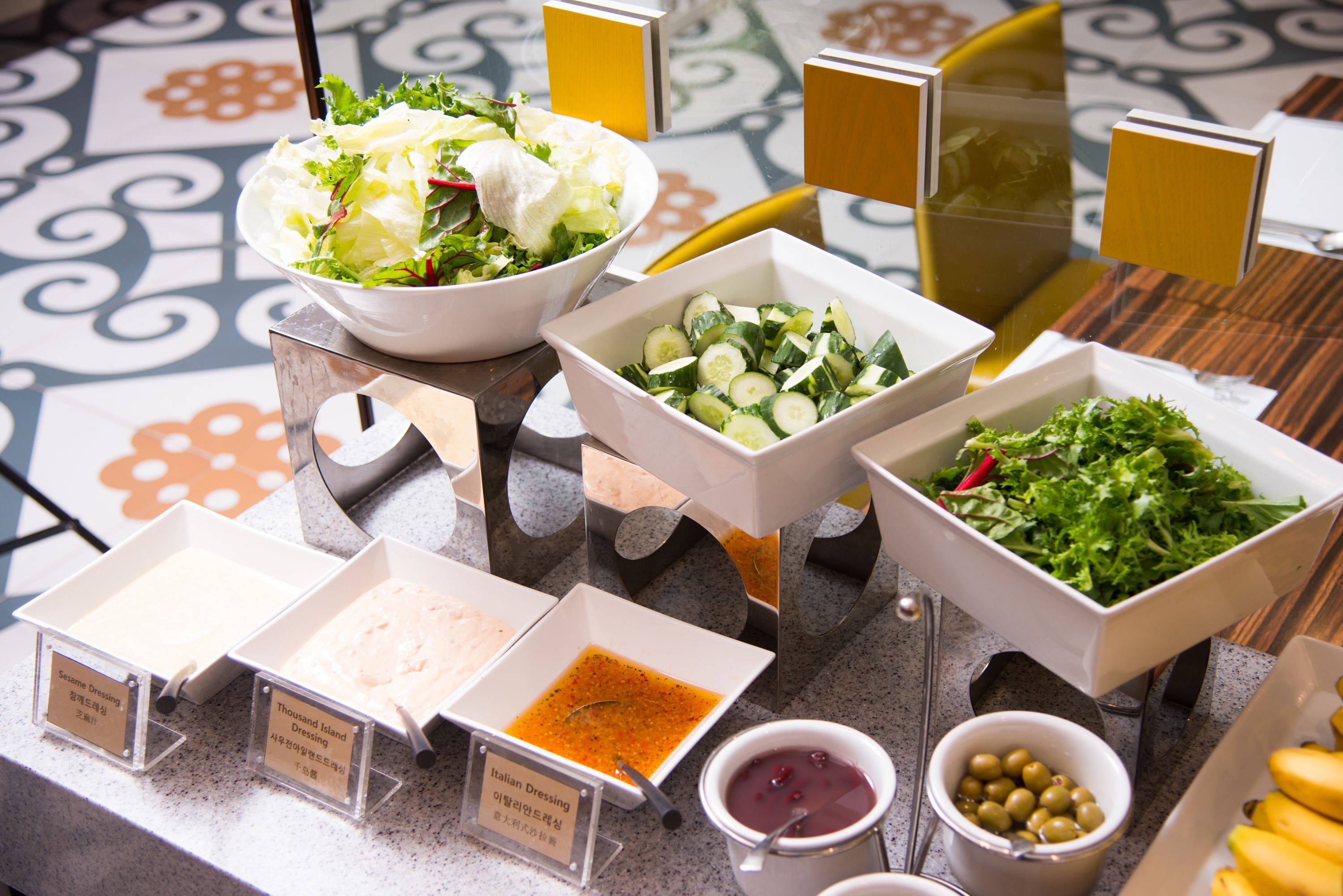 Un bufé con diversas opciones de comida, incluyendo ensaladas, aderezos y un bol de aceitunas.