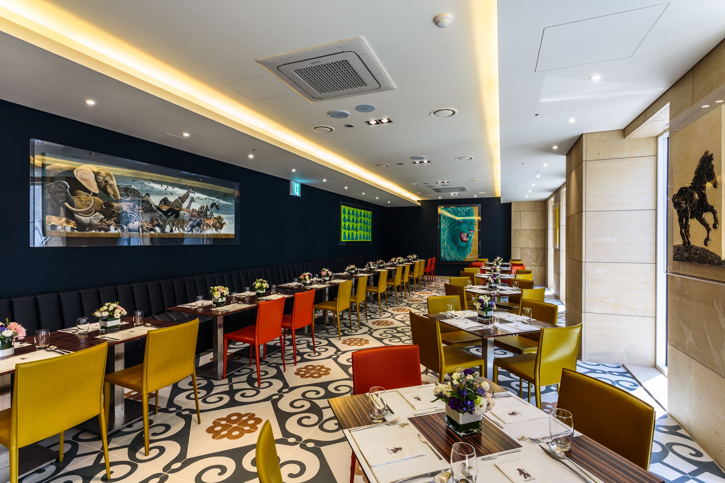 Un restaurante con una larga mesa común, mesas individuales y sillas en amarillo y rojo.