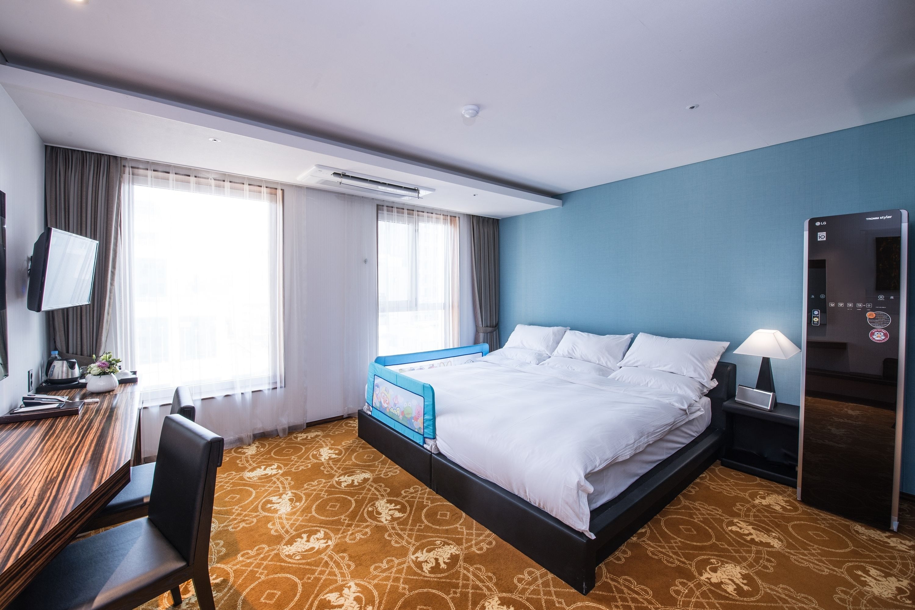 Habitación de hotel con cama, escritorio, silla y televisor en la pared.