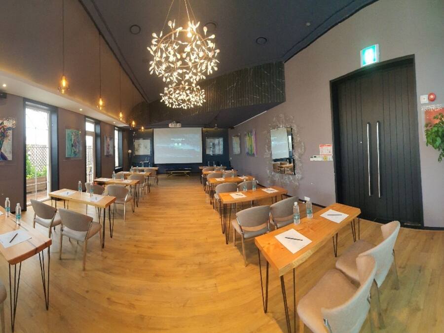 Un salón de conferencias con mesas y sillas de madera, una pantalla grande y un proyector.