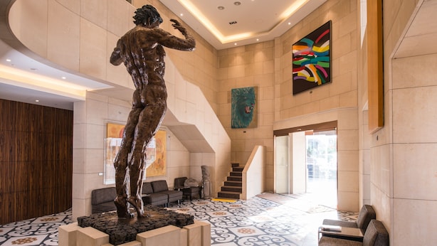 A lobby with a large bronze statue, a staircase, and a colorful abstract painting. - Hotel Leo (Jeju City)