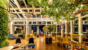 An indoor space with wooden flooring, tables, chairs, and a variety of plants. - Hotel Leo (Jeju City)