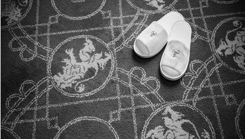 Un par de zapatillas blancas con un pequeño logotipo en la suela, sobre un tapete oscuro con diseños circulares y geométricos.