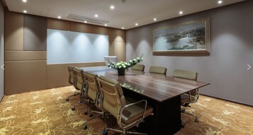 A conference room with a large table, six chairs, a projector screen, and a painting on the wall.