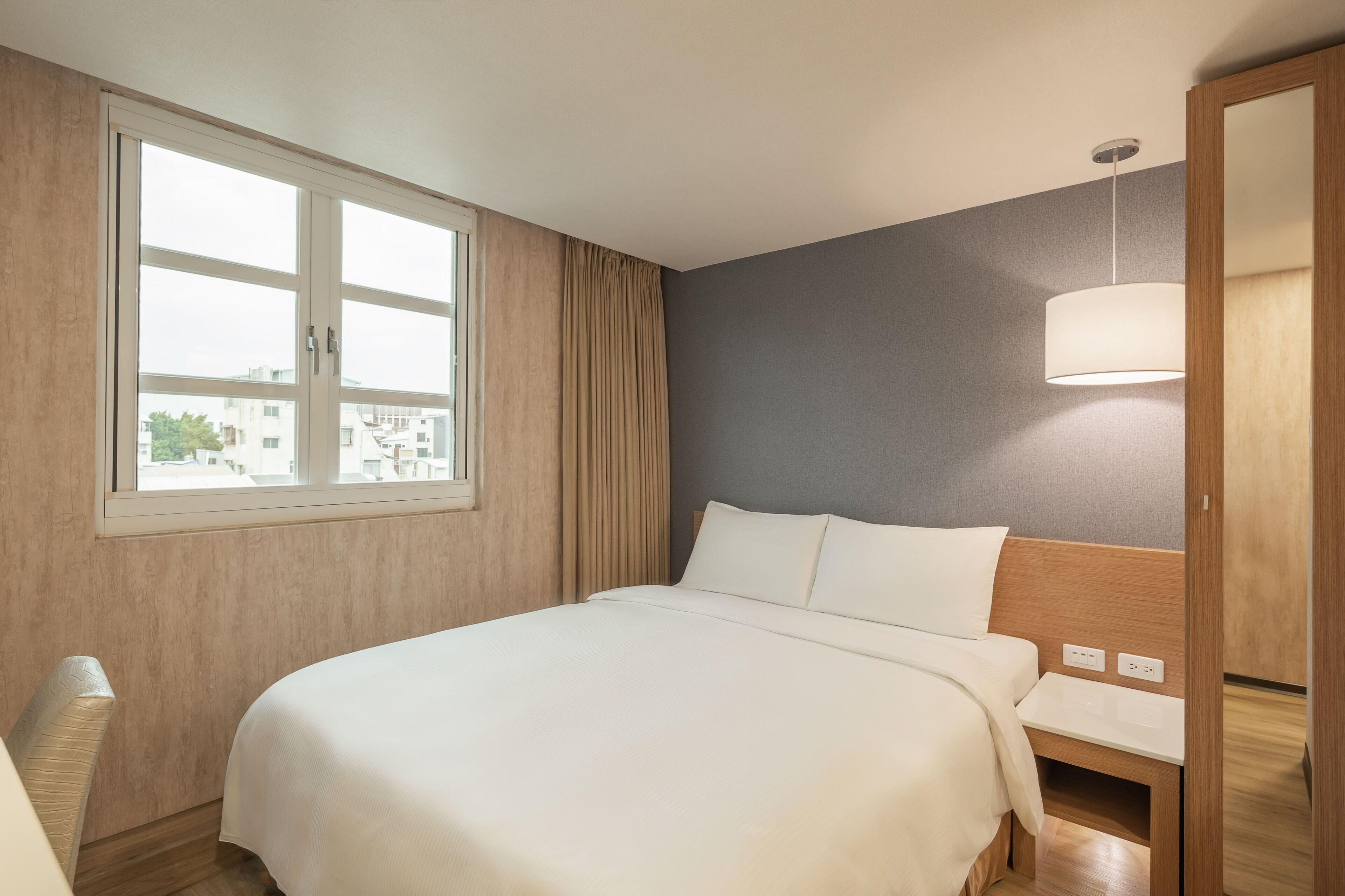 A hotel room with a large bed, a bedside table, a lamp, and a window with curtains.