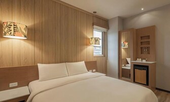 A bedroom with a wooden headboard, a bed with white linens, a bedside table, a nightstand, a wardrobe, and a window with a view.