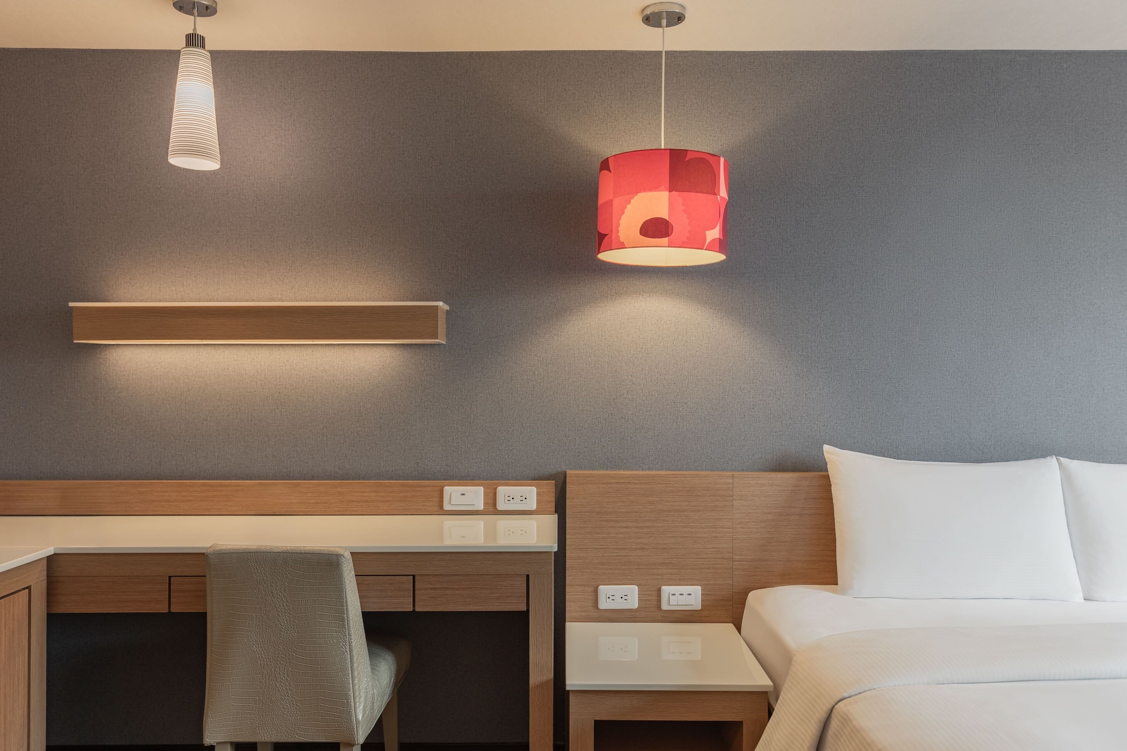 Habitación de hotel con cama, escritorio con silla, mesita de noche y dos lámparas colgantes.