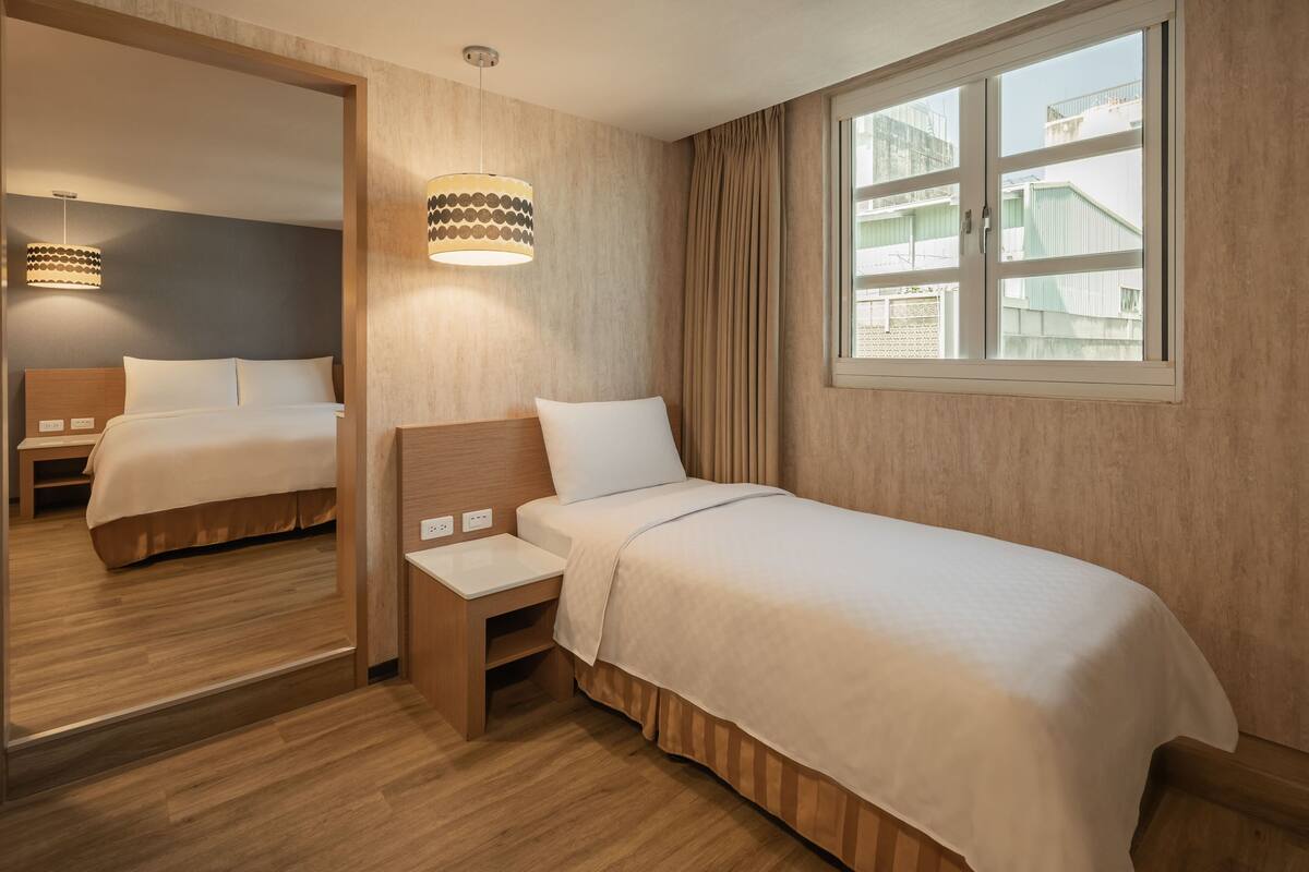 Ein Hotelzimmer mit Bett, Nachttisch, Spiegel, Fenster mit Vorhängen und einer Hängelampe.