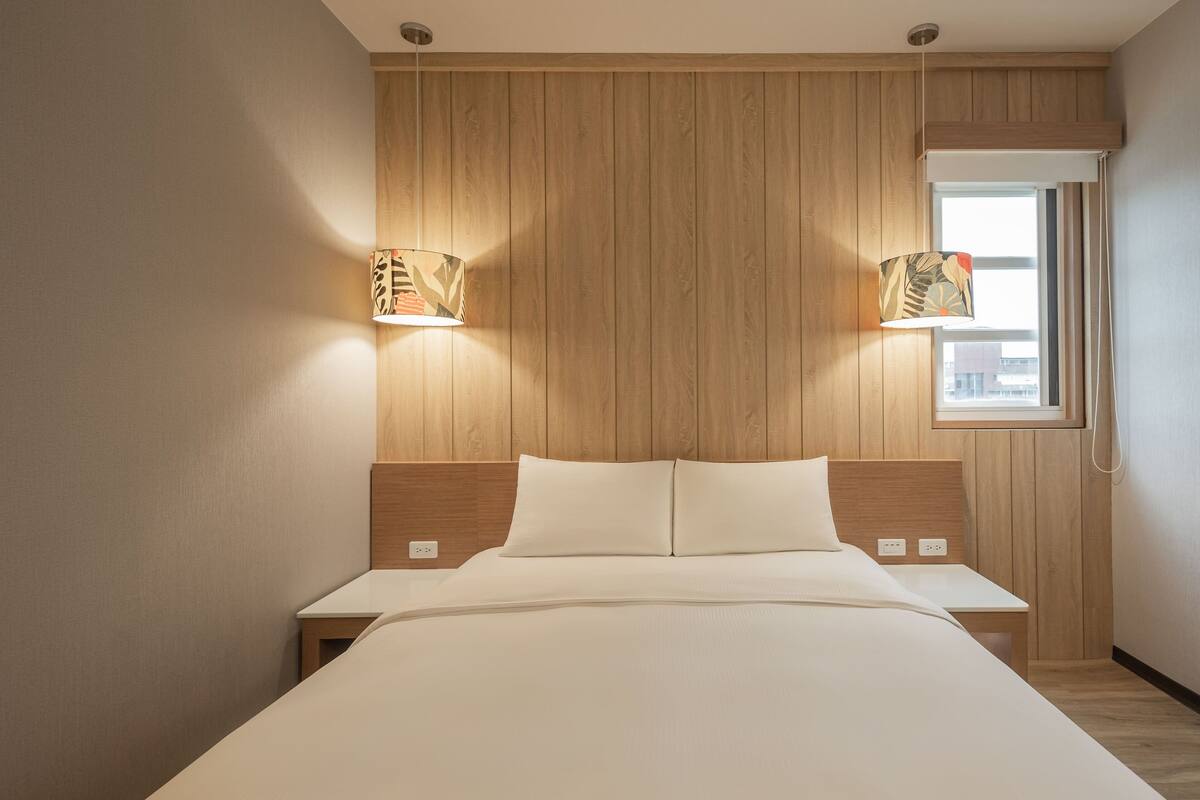 Ein Hotelzimmer mit einem hölzernen Kopfteil, einem großen Bett, Nachttischen und zwei Wandlampen.