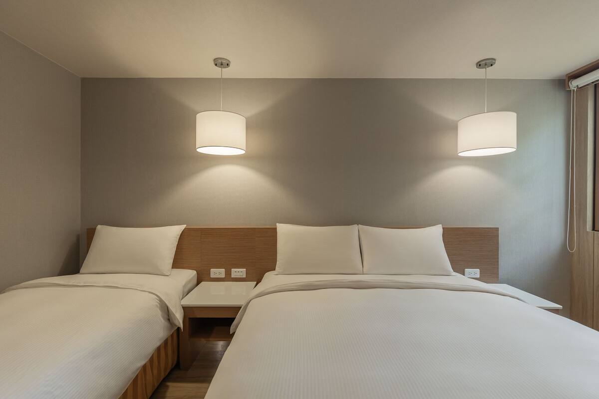 Ein Hotelzimmer mit zwei Betten, einem hölzernen Kopfteil, Nachttischen und zwei Pendelleuchten.