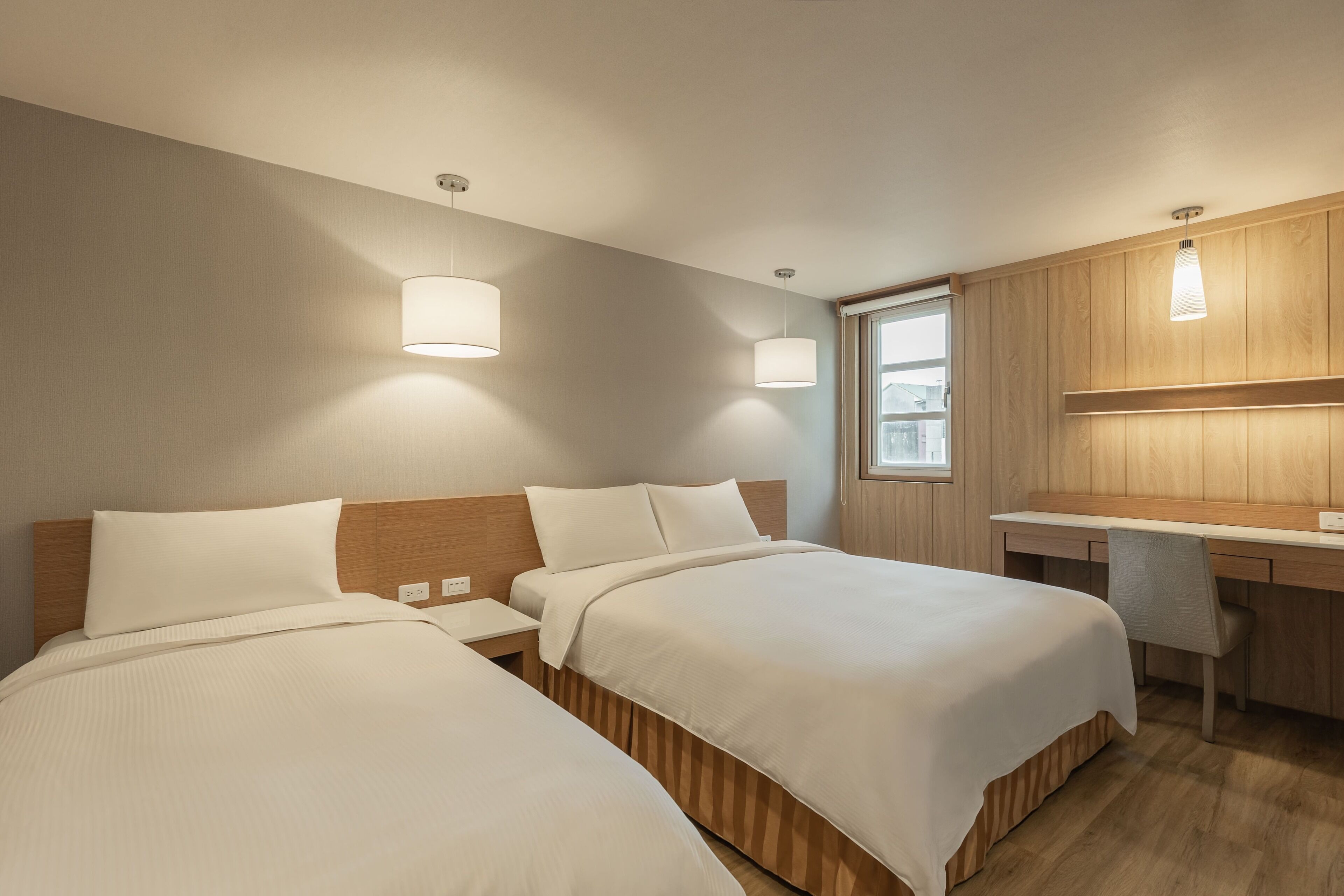 A hotel room with two beds, a desk, and a chair.