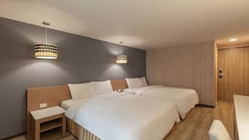 Habitación de hotel con dos camas, cabecero de madera, mesita de noche pequeña y dos lámparas colgantes.