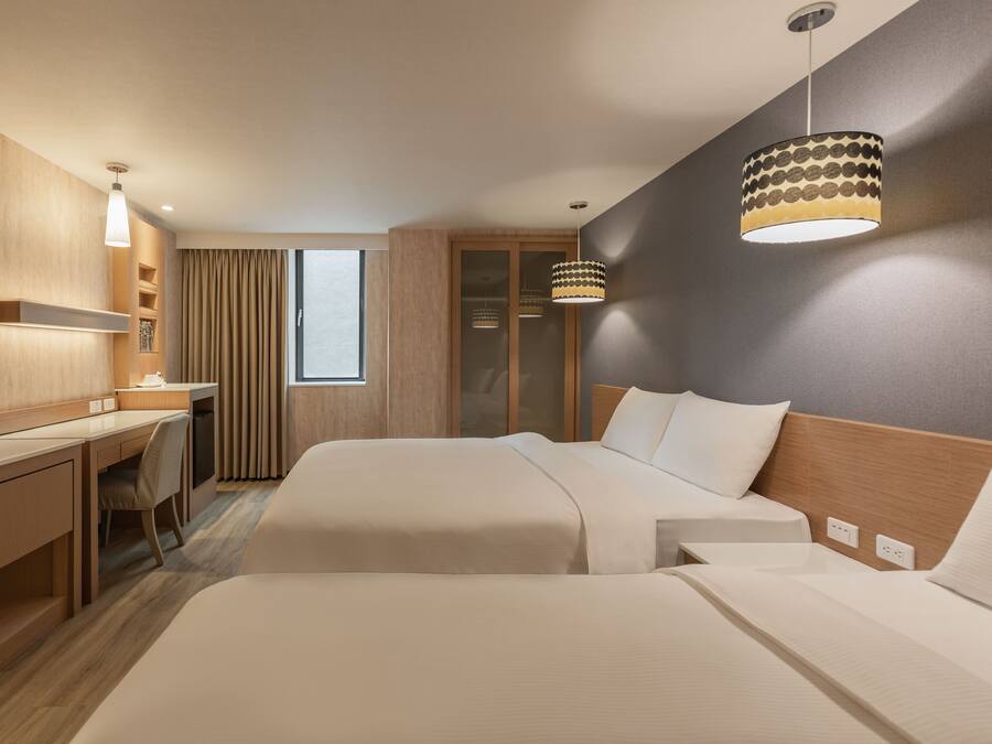 A hotel room with two beds, a desk, a chair, a TV, and a large window with curtains.