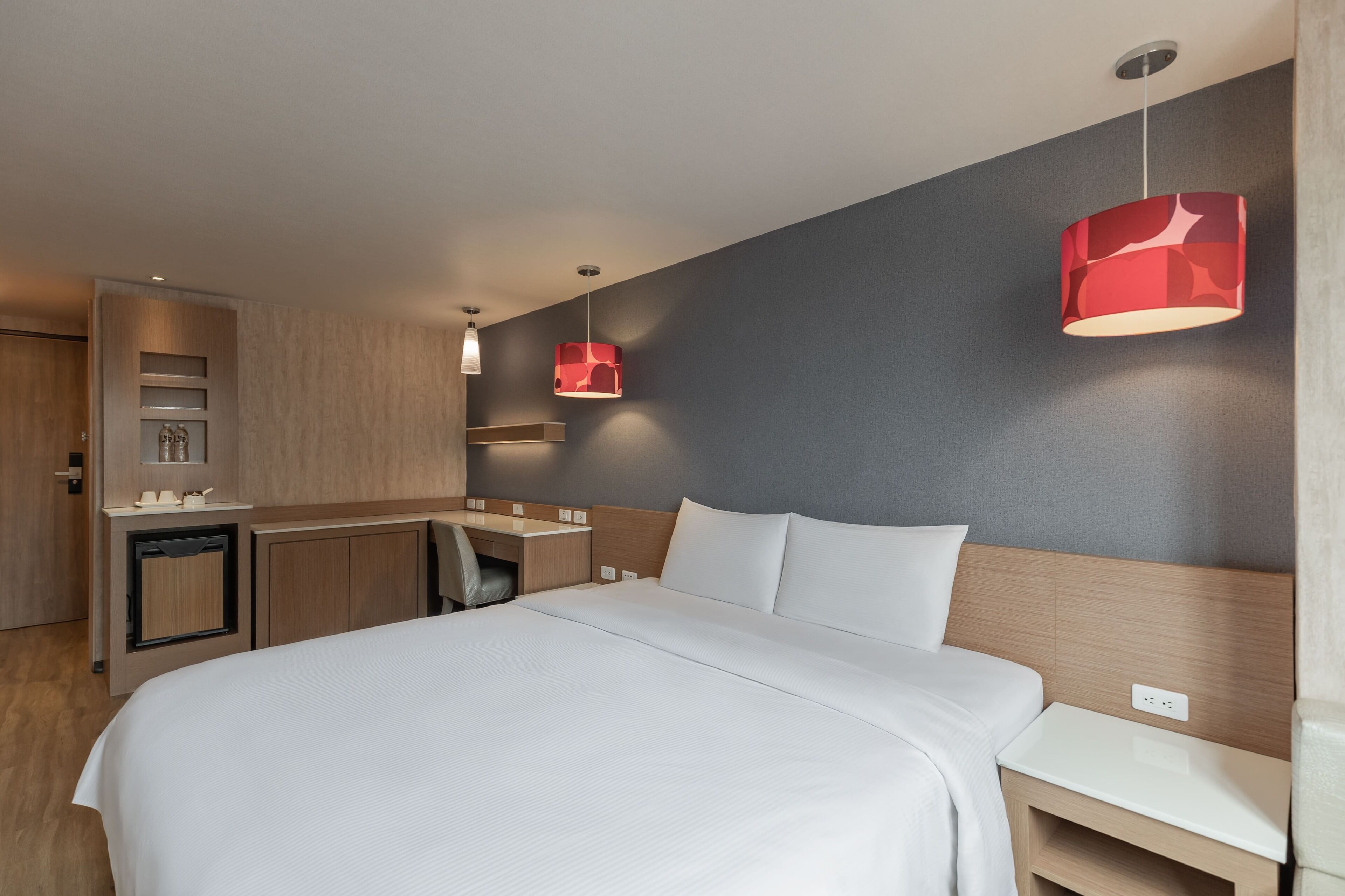 Una habitación de hotel moderna con una cama grande, un escritorio y una lámpara colgante roja.