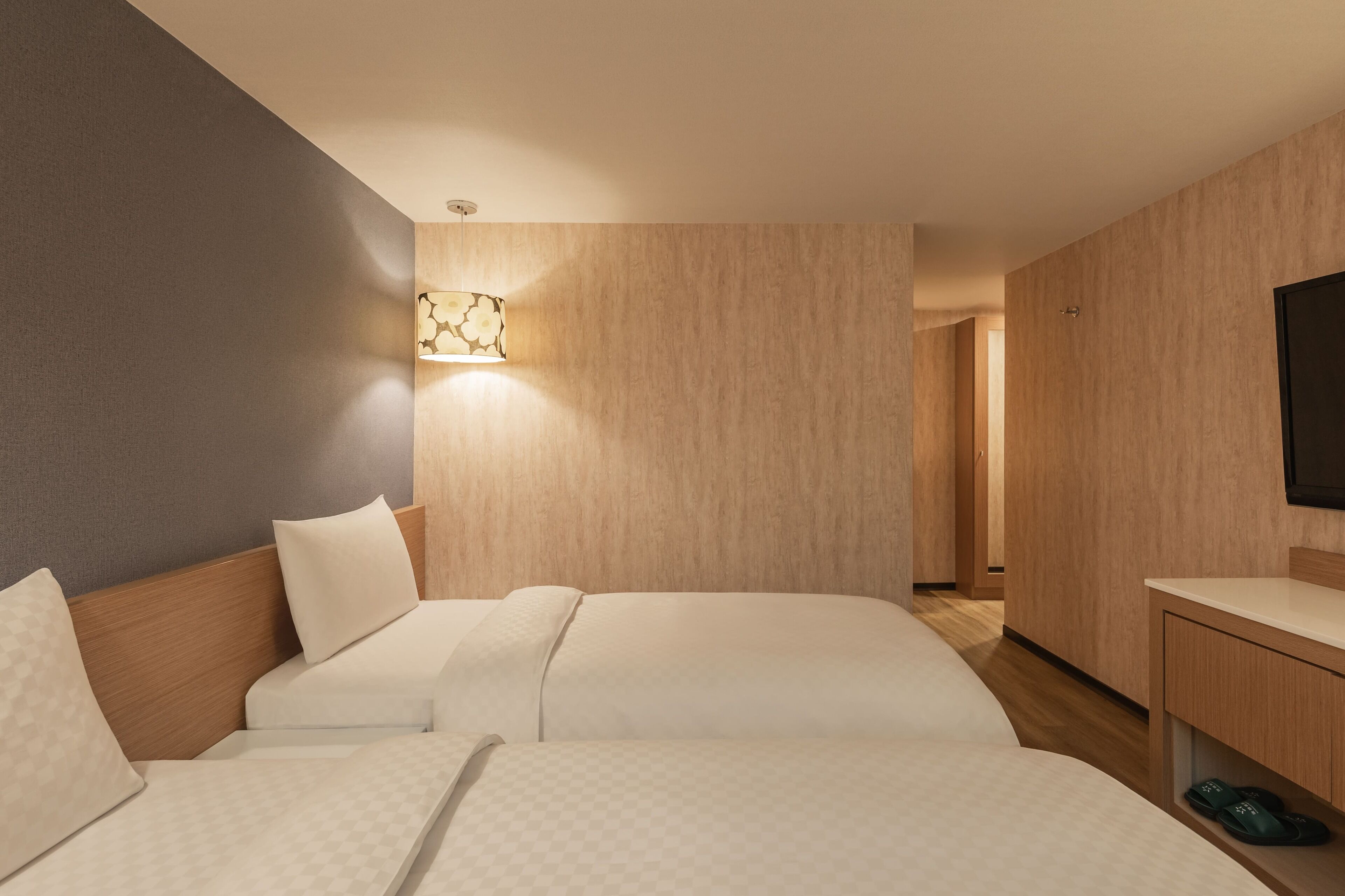 A hotel room with two beds, a bedside table, a TV, and a wall-mounted lamp.